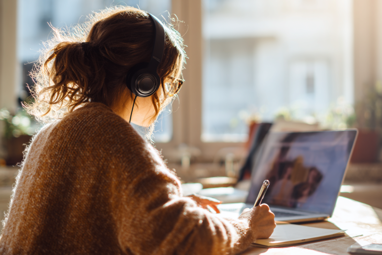 Person in gelbem Pullover hält Kopfhörer vor einem Laptop, mit Text “Das Webinar zur E-Rechnung” im Vordergrund.