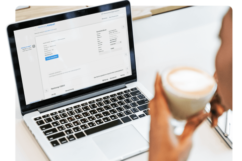 Person nutzt easybill Software zur Erstellung von Rechnungen auf einem Laptop, mit detaillierter Ansicht des Rechnungsentwurfs und einer Tasse Kaffee in der Hand.