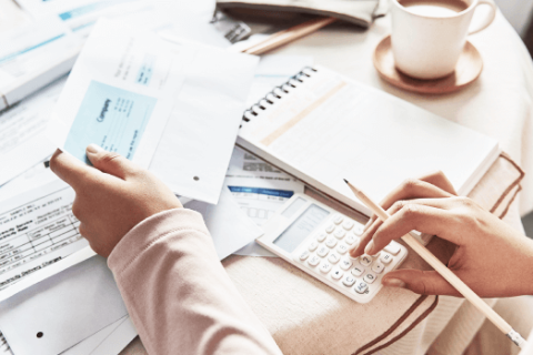 Person bei der Buchhaltung, die mit einem Taschenrechner und Rechnungen arbeitet, um die Mehrwertsteuer zu berechnen.